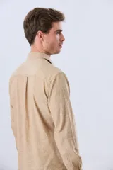 Camisa de lino de manga larga en color beige, con cuello camisero, cierre frontal de botones y un bolsillo ojal en el pecho.