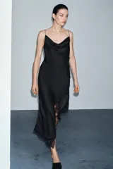 Vestido lencero de satén negro, corte midi asimétrico, con escote fluido y tirantes finos. Presenta drapeado lateral y aplicación de encaje a tono en el bajo.