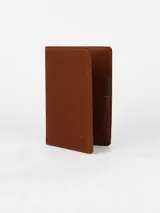Porta pasaporte de cuero color marrón, con costuras a tono y logo grabado en la parte inferior.