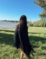 Ruana tejida a mano en lana merino, con diseño en V y terminación de flecos en el ruedo. Presenta una textura gruesa y una caída envolvente.