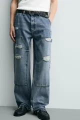 Pantalón de jean estilo carpintero con corte relaxed fit, tiro medio y pierna recta. Presenta un lavado azul medio con efecto desgastado y roturas en las rodillas. Incluye bolsillos laterales tipo plastrón, tira multifunción en la pierna, cierre frontal con cremallera y botón.
