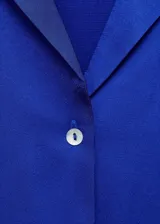 Camisa azul eléctrico de tejido satinado, manga corta, cuello camisero y cierre frontal con botones. Corte regular.