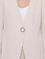 Blazer de sastrería color beige, sin solapas, con cuello en V profundo y cierre frontal de un único botón circular metálico en contraste.