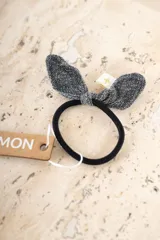 Gomita para el pelo negra con moño decorativo en forma de orejas de conejo, confeccionado en tela lurex plateada brillante.