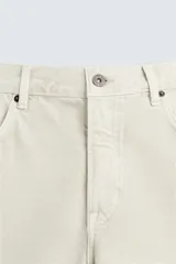Bermuda de denim de algodón color beige claro, de corte regular fit y largo hasta la rodilla. Presenta cinco bolsillos y cierre frontal con cremallera y botón.