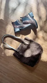 Bolso tipo tote de cuero con pelo color marrón y blanco, con manijas de cuero crudo.