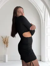 Minivestido negro de mangas largas, escote cuadrado con abertura en el abdomen y detalle de hebilla metálica. Falda ajustada con frunces laterales.