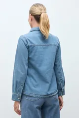 Camisa de jean de corte recto y calce relajado, con cuello clásico, cierre frontal con botones metálicos y dos bolsillos frontales con solapa.