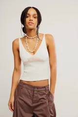 Musculosa de punto acanalado blanca, de calce ajustado y corto, con escote en V profundo, tiras finas y detalle de encaje en contraste bajo el escote.