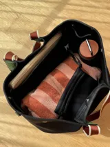 Bolso tipo tote de neopreno en color verde oliva, con correas de hombro en color rojo y detalles en blanco. Cuenta con broches imantados laterales para ajustar su forma y un bolsillo interno de red.