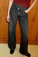 Jeans de tiro alto, color gris oscuro lavado, con pierna ancha extra larga (full length) y diseño de cintura cruzada asimétrica con cierre frontal de cremallera y botones metálicos.