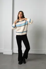 Buzo tejido de punto con diseño de guardas geométricas en tonos celeste y negro sobre base color crema. Presenta cuello redondo, mangas largas y puños acanalados.