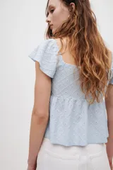 Blusa corta celeste de punto pointelle con textura, escote corazón, mangas cortas con vuelo y cordón de ajuste en el centro del busto.