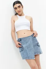 Minifalda de jean celeste con corte asimétrico, bolsillos de parche con solapa y tiras ajustables con hebillas en los laterales.