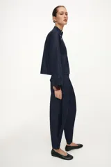 Pantalón de tiro alto confeccionado en denim oscuro, con pinzas delanteras que aportan volumen y pernera abullonada. Cuenta con bolsillos frontales, falsos bolsillos traseros con solapa y bajo ajustable mediante botones a presión.