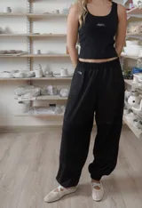 Pantalón negro de corte holgado y diseño abombacho, con cintura elástica fruncida, costuras decorativas y paneles en la parte inferior.