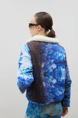 Campera con estampado de bosque en tonos azules, cuello de sherpa en color crema y cierre frontal con cremallera. Cuenta con elástico ajustable en la cintura.