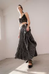 Pollera larga de corte amplio, confeccionada en tela con textura arrugada y acabado satinado, color negro. Presenta una cintura ancha y elástica que se ajusta al cuerpo.