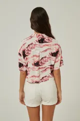 Camisa de corte cropped y manga corta con cuello camisero y cierre frontal de botones. Presenta un estampado abstracto tipo mármol en tonos rosados y negros, con dos bolsillos frontales.