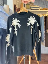 Buzo de punto negro con cuello redondo, manga larga y diseño de flores blancas bordadas en relieve en el frente y las mangas.