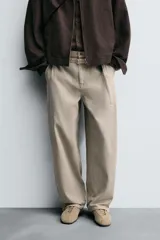 Pantalón de algodón color beige, estilo wide balloon fit, con cintura ajustable mediante cinturón de la misma tela. Presenta bolsillos frontales y bolsillos traseros de plastrón, con efecto lavado y abertura en el bajo.