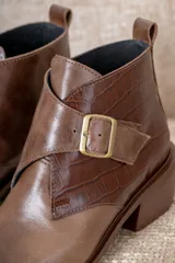 Botin de cuero negro con acabado brillante y detalle de solapa en cuero con textura de pelo, cierre con hebilla metálica lateral y punta fina.