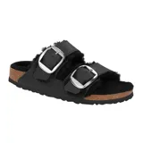 Sandalia Birkenstock modelo Arizona con forro de piel de oveja negra, dos correas anchas de cuero engrasado con hebillas grandes metálicas plateadas y suela de corcho con base de goma.