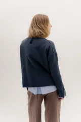 Buzo de lambswool color beige, con escote redondo y detalle en V. Presenta cierres metálicos en los puños que revelan un interior en contraste de color marrón y ribete rojo. Tiene tajos laterales para mayor comodidad y un fit amplio.