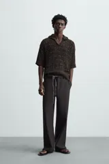 Polo de punto de calce relajado, color marrón oscuro jaspeado con negro. Presenta cuello solapa con abertura frontal en V y mangas cortas.