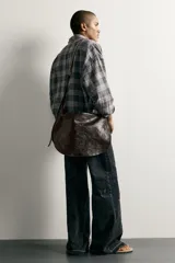 Bolso bandolera de piel color marrón oscuro, con diseño flexible y solapa frontal. Cuenta con asa larga ajustable y compartimento principal con bolsillo interior con cierre.