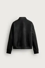 Campera bomber color verde militar de corte relaxed fit, confeccionada en tejido efecto ante, con cuello, puños y dobladillo en rib elástico, bolsillos frontales de vivo y cierre central con cremallera.