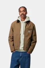 Campera Carhartt WIP modelo Detroit Jacket, de color marrón con cuello corduroy negro y cierre frontal de cremallera. Presenta un bolsillo con cierre en el pecho con el parche del logo de la marca.