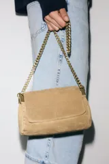 Bolso de hombro confeccionado en piel de gamuza color marrón, con diseño estructurado y pespuntes decorativos en la solapa. Cuenta con una correa de cadena metálica dorada con refuerzo de piel y cierre imantado.