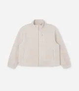 Campera deportiva de sherpa color beige, con cuello alto, cierre frontal completo y bolsillo con cierre en el pecho. Presenta un corte boxy holgado, mangas largas y acabado de textura suave.