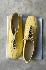 Zapato tipo flat de cuero amarillo con cordones frontales y punta cuadrada.