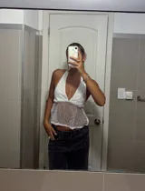 Top halter blanco con escote pronunciado en V, confeccionado en tejido transparente con lentejuelas o brillos plateados. La parte superior del busto es opaca y el resto del cuerpo es traslúcido.