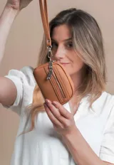 Monedero negro de diseño compacto con textura granulada, cuenta con doble compartimento principal con cierre y un bolsillo frontal adicional con cierre. Incluye una correa de mano extraíble.