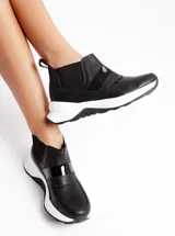 Sneakers negras de cuero vacuno con elásticos laterales y suela blanca de goma antideslizante.