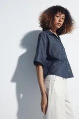 Camisa crop color blanco confeccionada en mezcla de lino, con cuello solapa, escote en pico, mangas cortas con trabilla, bolsillos de plastrón en el pecho y cierre frontal con botones.