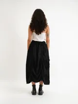 Pollera midi de diseño desestructurado en color negro, con cintura elastizada y detalles fruncidos con cordones ajustables a los lados.