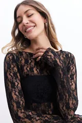 Remera negra de encaje floral con mangas largas, cuello redondo y corte ajustado. Incluye una capa interior opaca en el área del busto.