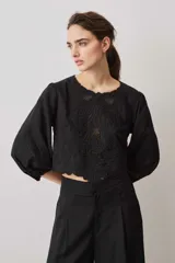 Blusa negra con detalles de apliques bordados en el pecho y las mangas, cuello redondo y mangas largas abullonadas.