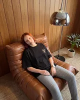 Remera negra de corte oversize, con estampa circular en la espalda que presenta la palabra 'Presente' en tipografía gótica de color beige.