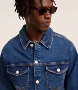 Campera trucker de jean azul oscuro, con cuello tradicional, cierre frontal con botones, cuatro bolsillos y mangas largas.