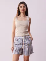 Short color crema con finas rayas verticales grises, pretina elastizada con cordón de ajuste, bolsillos delanteros y traseros.