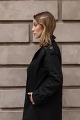 Trench clásico de largo midi en color beige, con diseño de doble abotonadura, solapas amplias, detalles en hombros y correas ajustables en los puños.