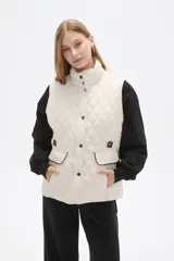 Chaleco acolchado de diseño capitoneado en color verde militar, con cuello alto, cierre frontal con botones a presión y bolsillos laterales con solapa y detalles en contraste.