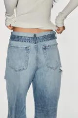 Jeans de mezclilla de tiro medio, corte wide leg y diseño relaxed. Presenta detalles rotos y desgastados en las piernas, y una cinturilla doblada superpuesta con trabillas y cierre frontal con cremallera y botón metálico.