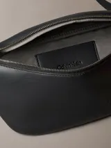 Riñonera Calvin Klein negra de poliuretano, diseño waist bag con cierre de cremallera superior, correa ajustable y monograma CK grabado en la parte delantera.
