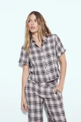 Camisa de manga corta con cuello camisero y botones frontales. Presenta un estampado de cuadros escoceses en tonos marrón oscuro y blanco/beige, con un calce entallado.